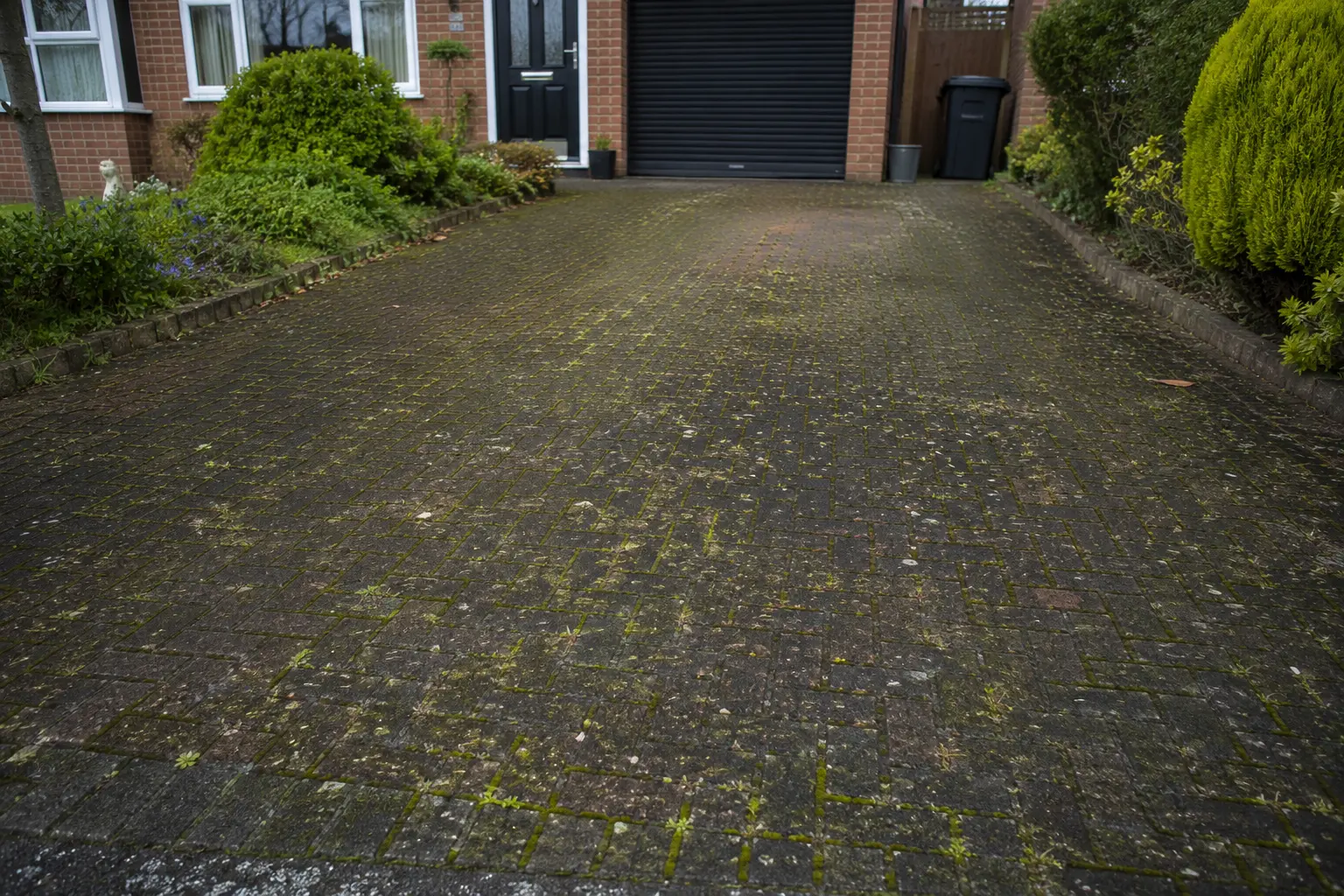 Driveway Cleaning Service Roof Cleaning Bournemouth Dirty block paving driveway covered in moss and weeds outside a residential home in Bournemouth.
